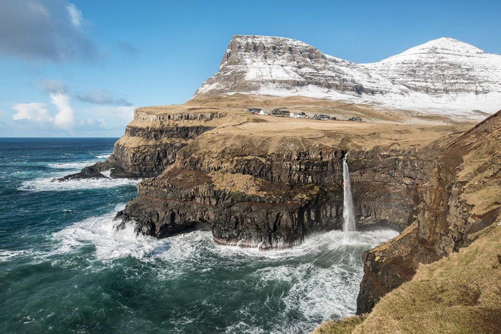 Vodopád Múlafossur u vísky Gásadalur na Faerských Ostrovech. A se sněhem pocukrovanými vrcholkami na pozadí